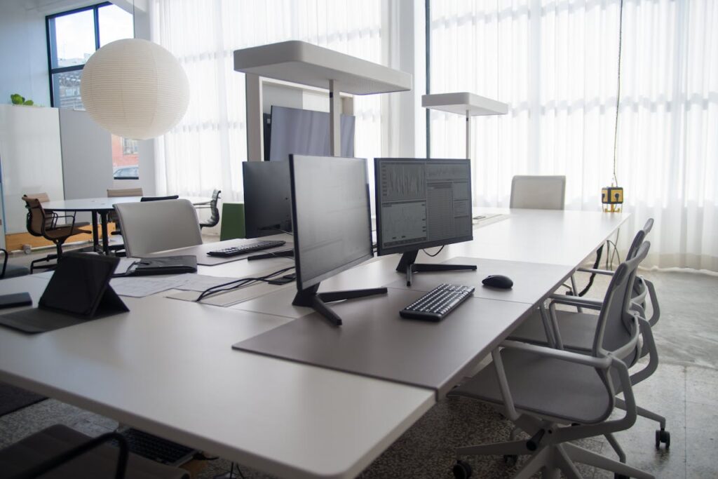 Spacious modern office featuring multiple computers, chairs, and collaborative workstations in natural light.