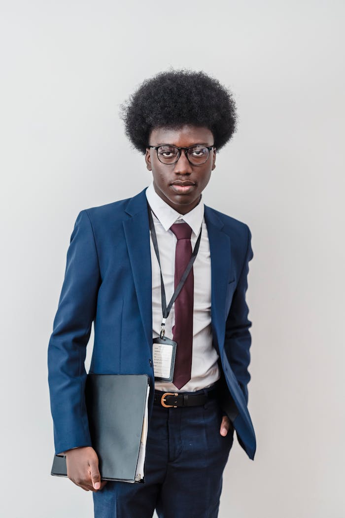 Confident young businessman in formal suit with afro hairstyle holding document, white background.