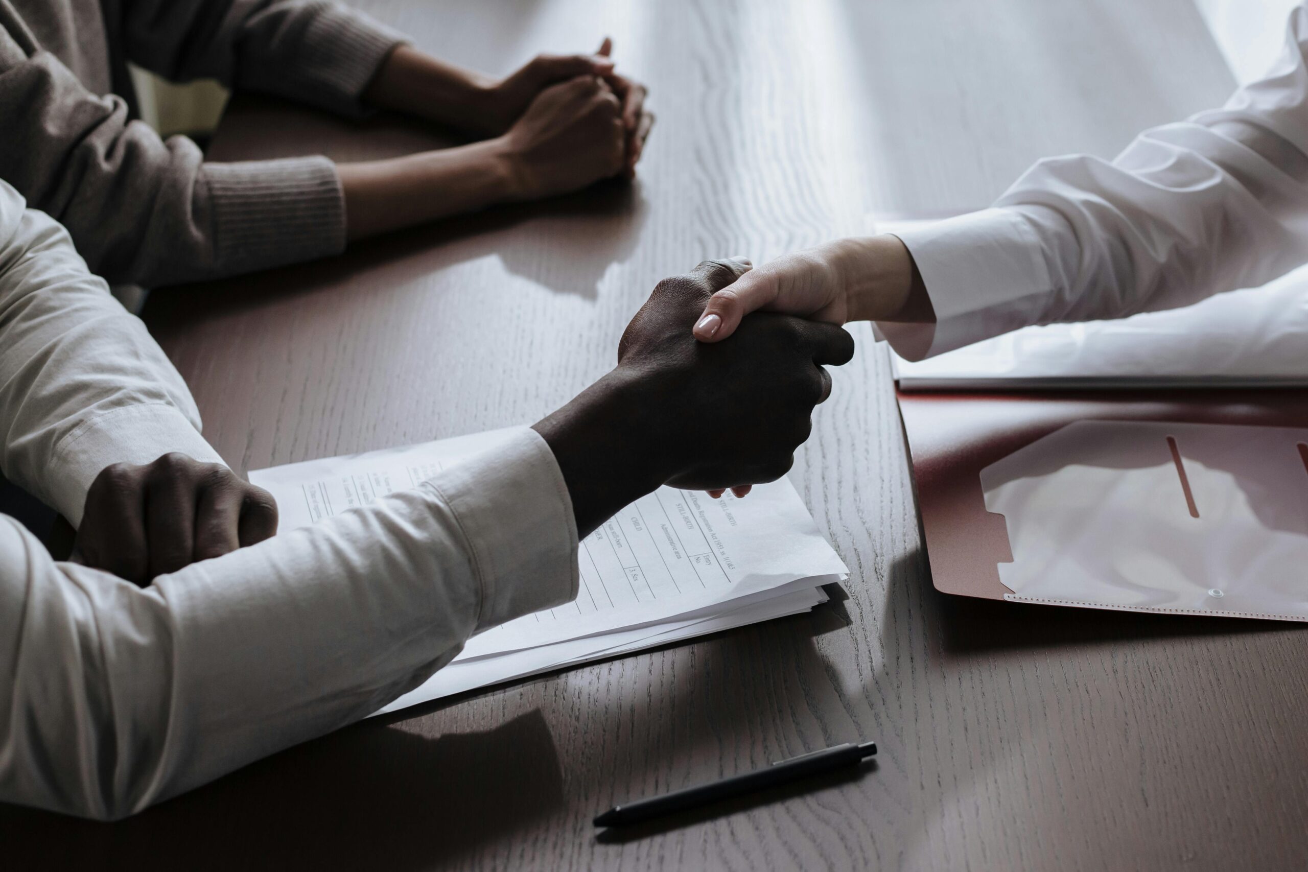 Business agreement with a handshake over contract documents at a meeting table.